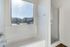 Bright bathroom with large window, featuring a luxurious bathtub and modern shower, offering serene views of the neighborhood.