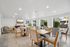 Bright and elegant community dining room with modern wooden furniture, large windows showcasing lush greenery, and a sleek mounted TV for an inviting atmosphere.
