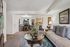 Elegant living room with cozy seating, a stylish glass coffee table, and a view into a chic dining area, featuring modern decor and warm lighting.