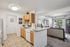 Bright apartment kitchen with modern white countertops, wooden cabinets, and seamless flow into a cozy living area with elegant decor and large windows.