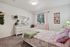 Charming bedroom with soft pastel decor, featuring a cozy bed with patterned bedding, a white dresser with a mirror, and an abundance of natural light from the window with pink curtains.