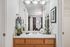 Elegant bathroom vanity with wooden cabinets, chic decor, and a large mirror reflecting natural light from a nearby room.