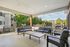 Inviting covered patio with modern outdoor seating overlooking a peaceful apartment complex and lush green surroundings.