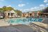 Inviting outdoor pool area with stylish sun loungers, brick cabanas, and lush surrounding greenery under a bright blue sky.