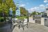 Charming outdoor patio with seating and barbecue area, surrounded by lush greenery and bright blue skies.