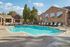Stunning community pool area surrounded by inviting sun loungers, lush greenery, and charming brick architecture under a bright blue sky.