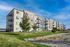 Modern apartment complex with stylish balconies, lush green surroundings, and a clear blue sky backdrop.