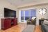 Chic living room with stylish decor, featuring a sleek TV on a vibrant red media console, a cozy armchair, and a panoramic city view through large glass doors.