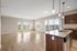 Bright open-concept living area featuring a modern kitchen with granite countertops and wood flooring, overlooking a serene outdoor view through large windows.