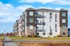 Modern Aspen Lofts apartment building with vibrant facade, multiple balconies, and beautiful landscaping under a clear blue sky.