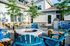 Inviting patio area with vibrant blue chairs surrounding a cozy fire pit, complemented by lush greenery and a modern barbecue setup.