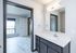 Bright and modern bathroom featuring sleek cabinetry, a large mirror, and a view into a sunlit room with elegant flooring.