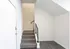 Bright modern entryway with sleek white walls, elegant gray carpeted stairs, and stylish black railing.