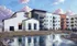 Modern apartment complex with stylish design, featuring balconies and a serene pond with a fountain, under a vibrant sky.