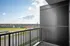 Inviting balcony view overlooking a vibrant neighborhood with stores and green spaces under a bright blue sky.