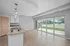Bright and modern open-plan kitchen and living area featuring hardwood floors, granite countertop island with sink, and large windows offering a scenic street view.