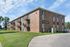 Inviting brick apartment building with private balconies, set against a serene green lawn and clear blue sky.