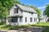 Charming two-story home with classic white siding, abundant natural light, and lush green surroundings.