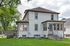 Charming two-story home with a spacious front porch, surrounded by lush greenery and mature trees.