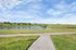 Scenic view of a serene pond surrounded by green fields and a walking path under a bright blue sky.