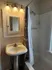 Charming bathroom with elegant lighting, sleek pedestal sink, and classic tiled shower for a comfortable living space.