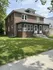 Charming brick duplex with inviting front porch and lush green lawn, bathed in sunlight on a serene suburban street.