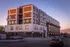 Modern, multi-story apartment building with elegant design, large windows, and vibrant sunset reflections in the urban environment.