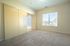 Bright bedroom with large window, plush carpet, and sliding closet doors in a modern apartment.