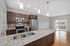 Modern kitchen with granite countertops, sleek stainless steel appliances, and elegant pendant lighting, opening to a bright living area with hardwood floors and a balcony view.