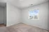 Bright and airy bedroom with soft carpet flooring and a large window offering a stunning view of neighboring buildings under a clear blue sky.