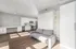 Modern open-concept living space featuring sleek kitchen with white cabinetry, integrated appliances, and a cozy gray sofa, enhanced by abundant natural light.