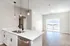 Bright modern kitchen with sleek white countertops, stylish pendant lighting, and open-concept living area leading to a balcony with scenic views.