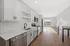 Modern kitchen with sleek white cabinetry, stainless steel appliances, and an open-concept design flowing into a sunlit living area.