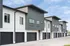 Modern multi-story townhouses with sleek design and spacious garages under a bright blue sky.