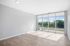 Bright and airy apartment room with large floor-to-ceiling windows offering a scenic view of greenery, complemented by sleek wood flooring and modern recessed lighting.