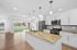 Bright, modern kitchen with granite countertops and stainless steel appliances, overlooking a spacious living area with large windows and natural light.