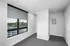 Modern apartment room with large window offering scenic views, featuring a spacious carpeted floor and sleek built-in closet.
