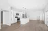 Modern open-plan kitchen with sleek white cabinetry, stainless steel appliances, and stylish pendant lighting, leading into a bright and spacious living area with wood flooring.