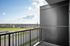 Charming balcony view overlooking a vibrant urban landscape with shops, green spaces, and distant houses under a bright blue sky.