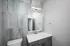 Modern bathroom featuring sleek gray cabinets, a pristine marble countertop, large mirror, and elegant gray wall tiles.