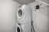 Modern laundry room featuring a sleek, stackable washer and dryer set, complemented by a convenient wall-mounted shelf.