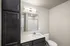 Modern bathroom featuring sleek dark cabinetry, elegant lighting, and a pristine white countertop with a built-in sink.