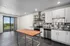 Modern kitchen featuring sleek cabinetry, stainless steel appliances, and a large wooden island, with a scenic view through sliding glass doors.