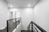 Modern staircase with sleek railing leads to bright hallway with open doors, showcasing a minimalist design.