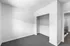 Bright, minimalist room with cozy carpet, open closet space, and modern railing in view.
