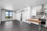 Modern open-concept apartment with sleek dark flooring, stylish kitchen, and large window offering scenic views.