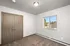 Bright bedroom with large window and double door closet, featuring neutral carpet and modern light fixture.
