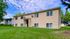 Charming suburban apartment building with a well-maintained exterior, set against a backdrop of lush green grass and mature trees.