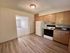 Bright kitchen with wooden cabinets, modern appliances, and open entry to a well-lit living area with carpeted floors.