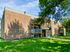 Charming brick apartment building with lush green lawn, shaded by mature trees, offering a serene and inviting atmosphere.